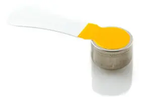 A close-up of a small round metal object with a flat, yellow and transparent plastic tab attached to the top, isolated on a white background.