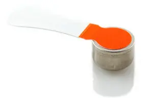 A round, silver battery is shown with a white tab that has an orange sticker on its end, covering the top of the battery.