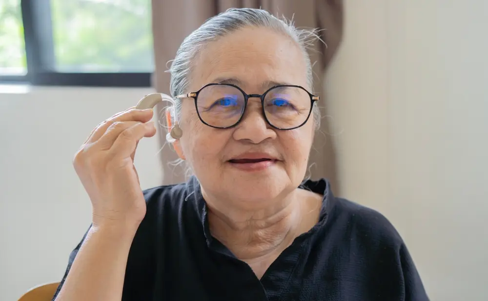 An older woman holding a pair of hearing aids