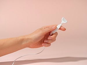 A hand holding a small white electric razor or trimmer against a light pink background.