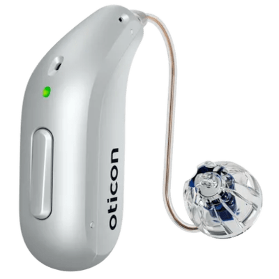 A silver hearing aid with a curved wire and a transparent earpiece. The device has a small green indicator light and the brand name Oticon printed vertically on its side.