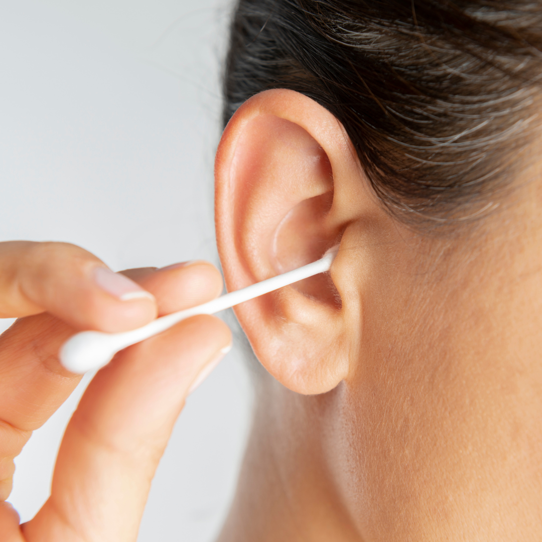 A person gently cleans the outer part of their ear with a cotton swab.