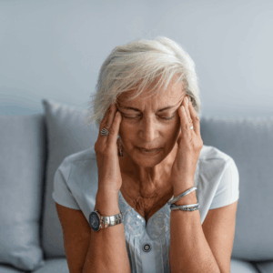 An older woman with silver hair holding her temples, looking as though she has a headache.