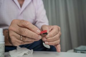 A person uses a small red tool to clean a hearing aid.