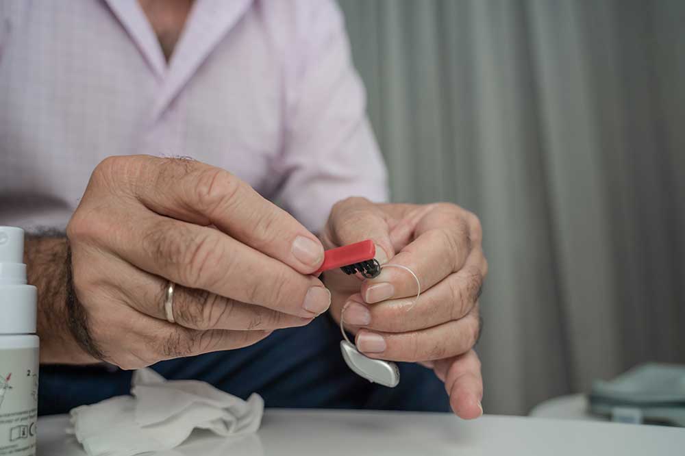 A person uses a small red tool to clean a hearing aid.