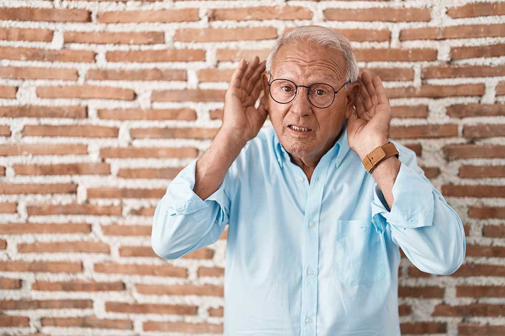 Older man in glasses cupping his hands behind his ears to hear, as when hearing aids sound uneven, from Aspire Hearing Solutions in Lakeland, FL