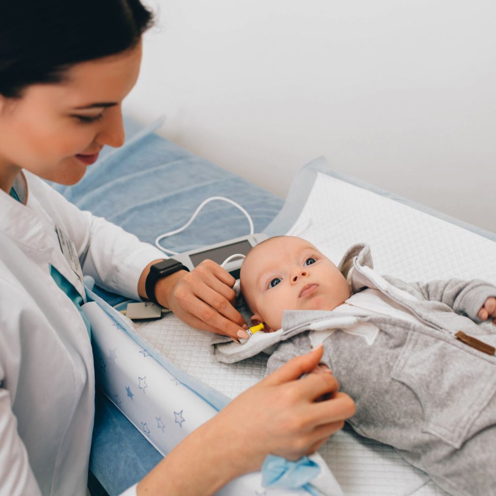 A healthcare professional performs a hearing screening on a baby lying on an exam table.
