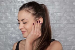 A woman with a ponytail touching her ear with dark purple nail polish.