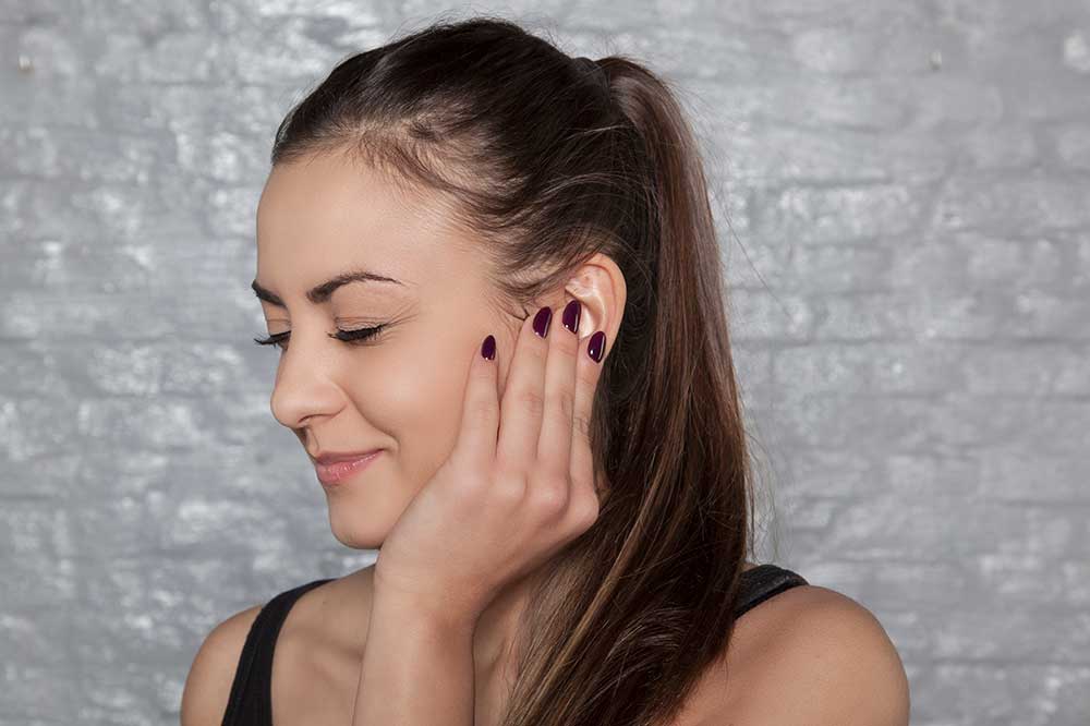 A woman with a ponytail touching her ear with dark purple nail polish.